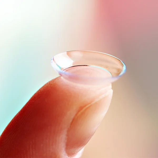 A fingertip with a contact lens sitting atop it