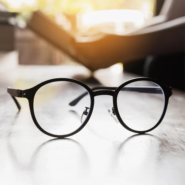 A polished wooden table with eyeglasses settled atop it
