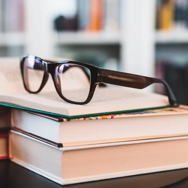 A pair of eyeglasses balanced atop a stack of books